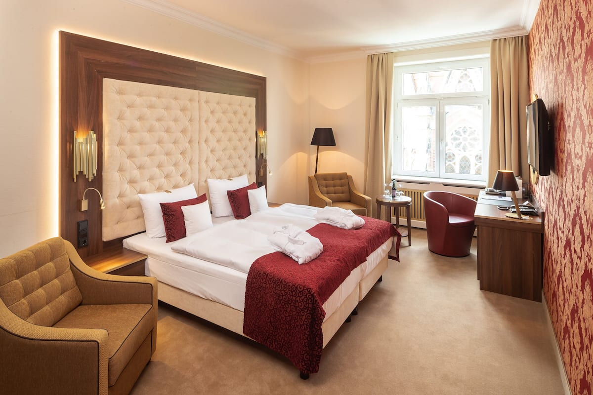 A hotel room with a large bed, two armchairs, a desk, and a window with curtains.