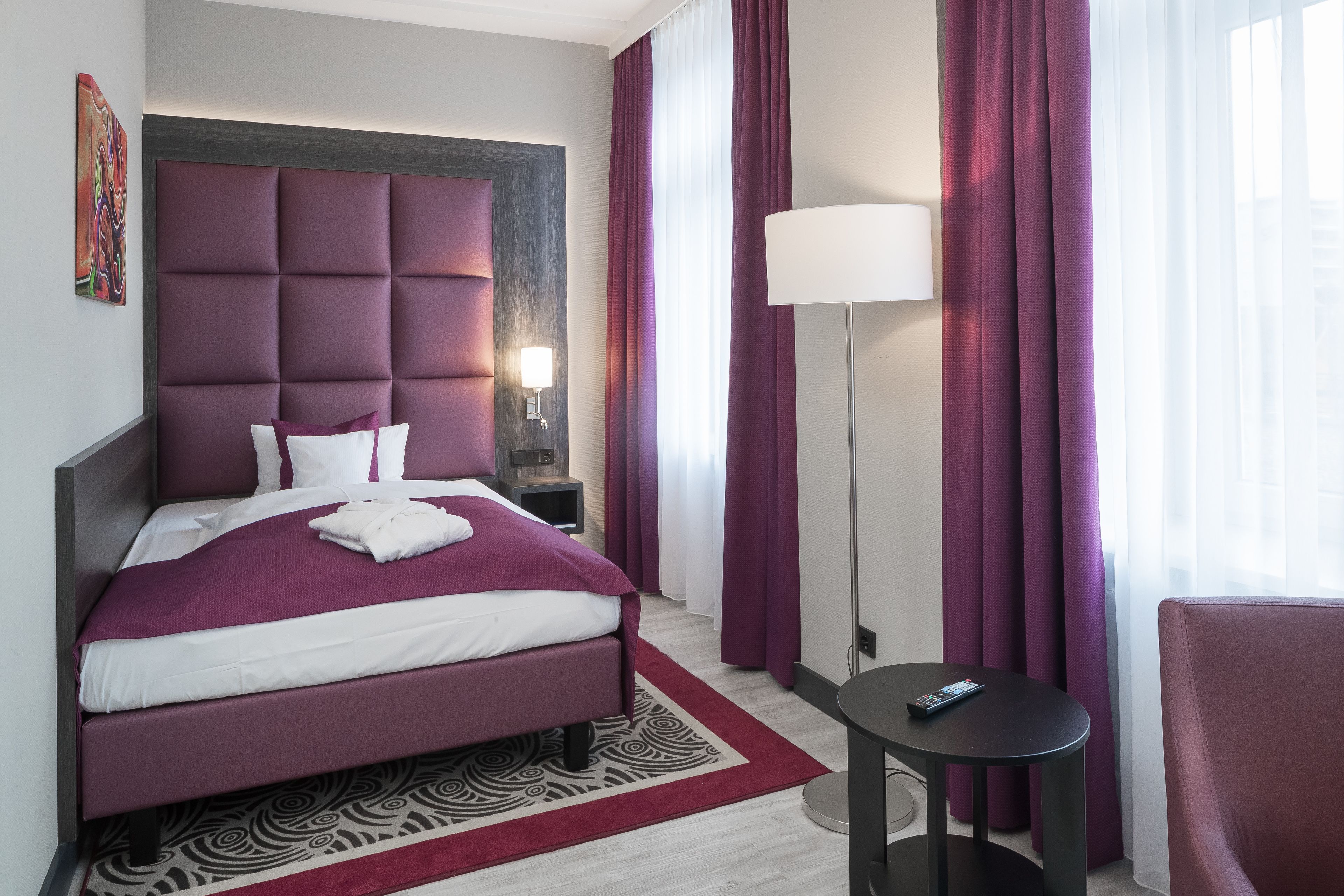A modern hotel room with a large bed, a bedside table, a lamp, and a chair.