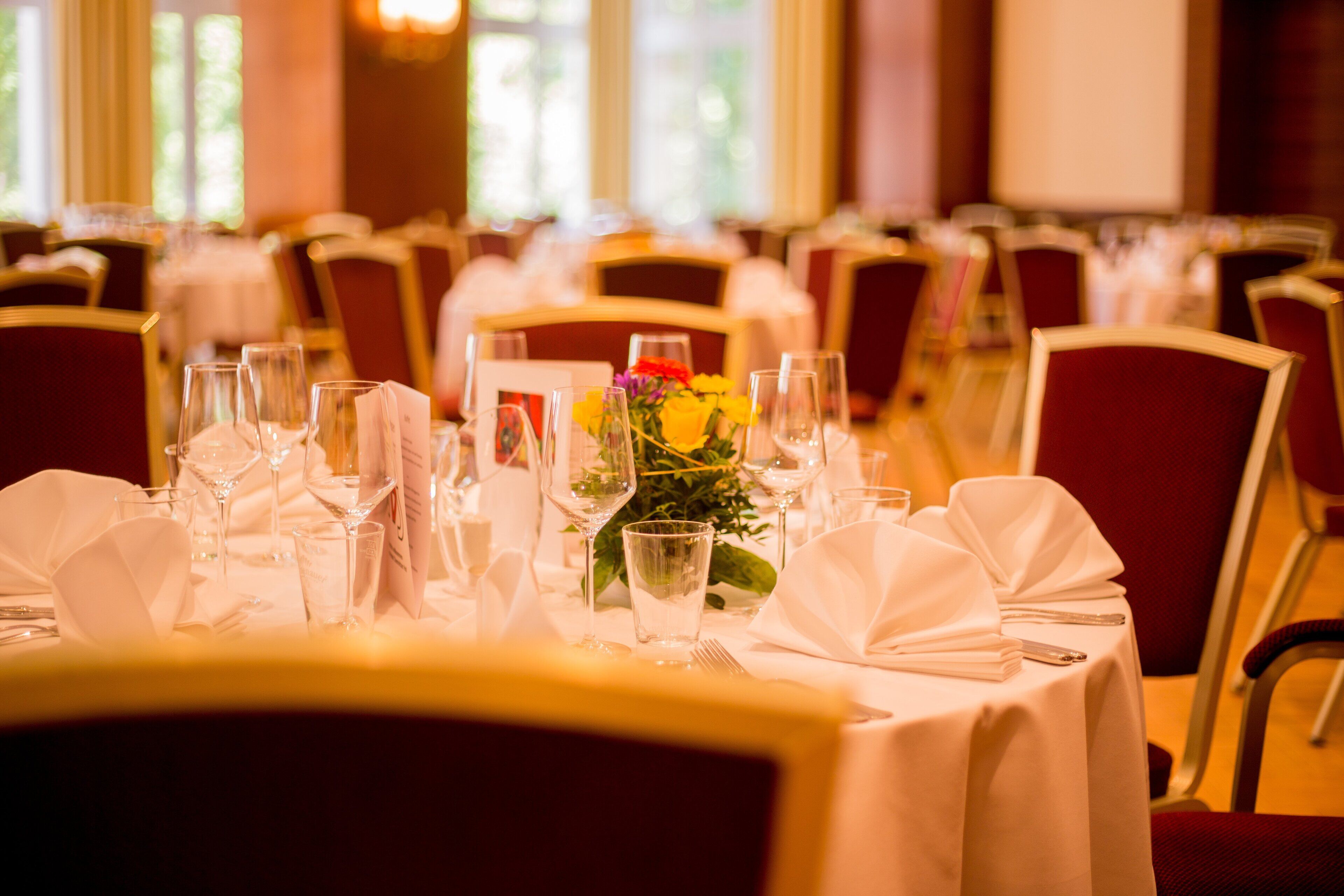 Une salle de banquet avec des tables dressées pour le repas, agrémentée de nappes blanches et de chaises rouges.