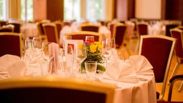 Une salle de banquet avec des tables dressées pour le repas, agrémentée de nappes blanches et de chaises rouges.
