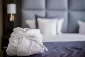 Un bata blanca doblada cuidadosamente sobre una cama con una colcha azul oscuro y un cabecero capitonado.
