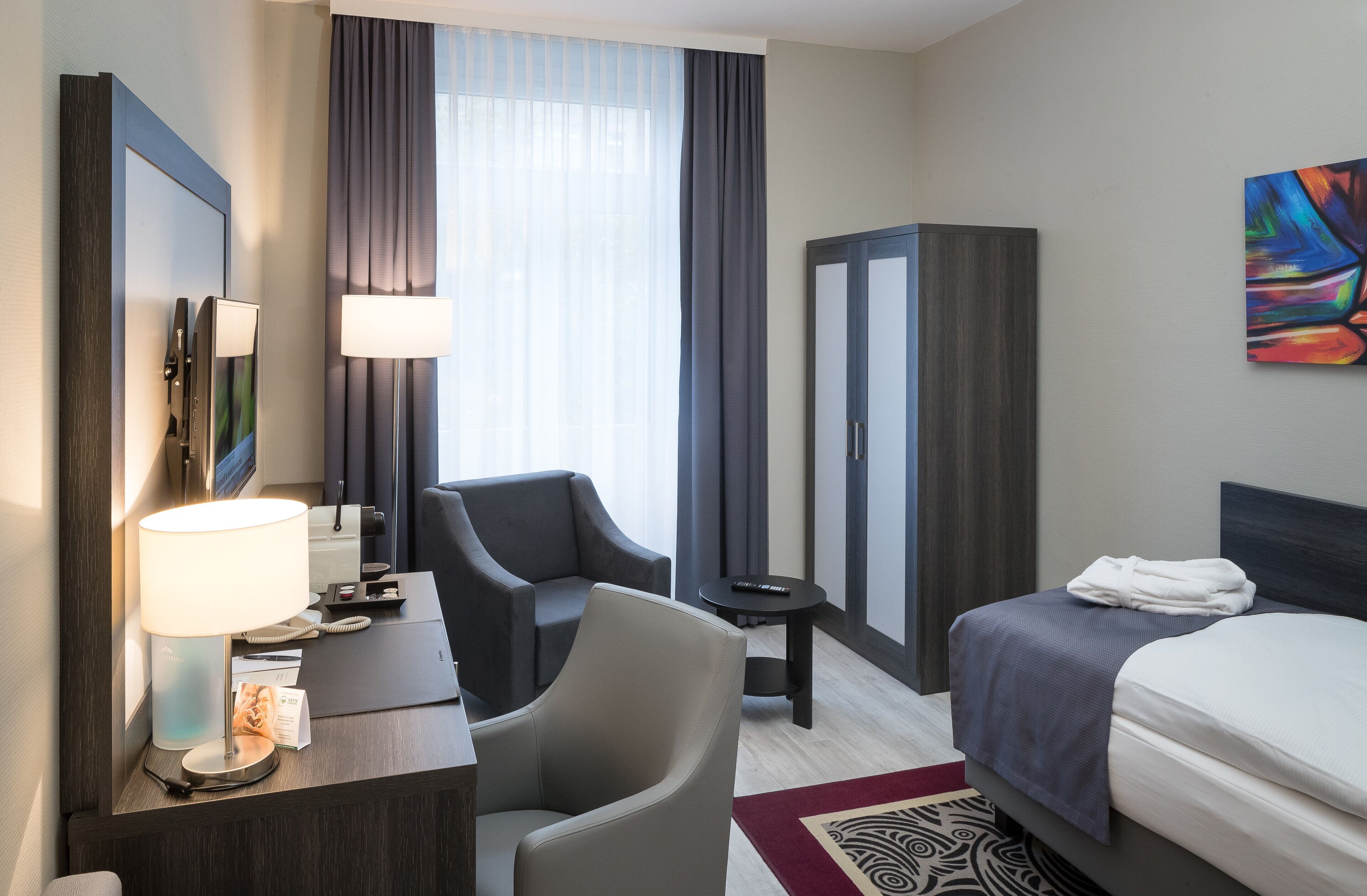 Une chambre d’hôtel équipée d’un bureau, d’une chaise, d’un lit et d’un grand miroir.