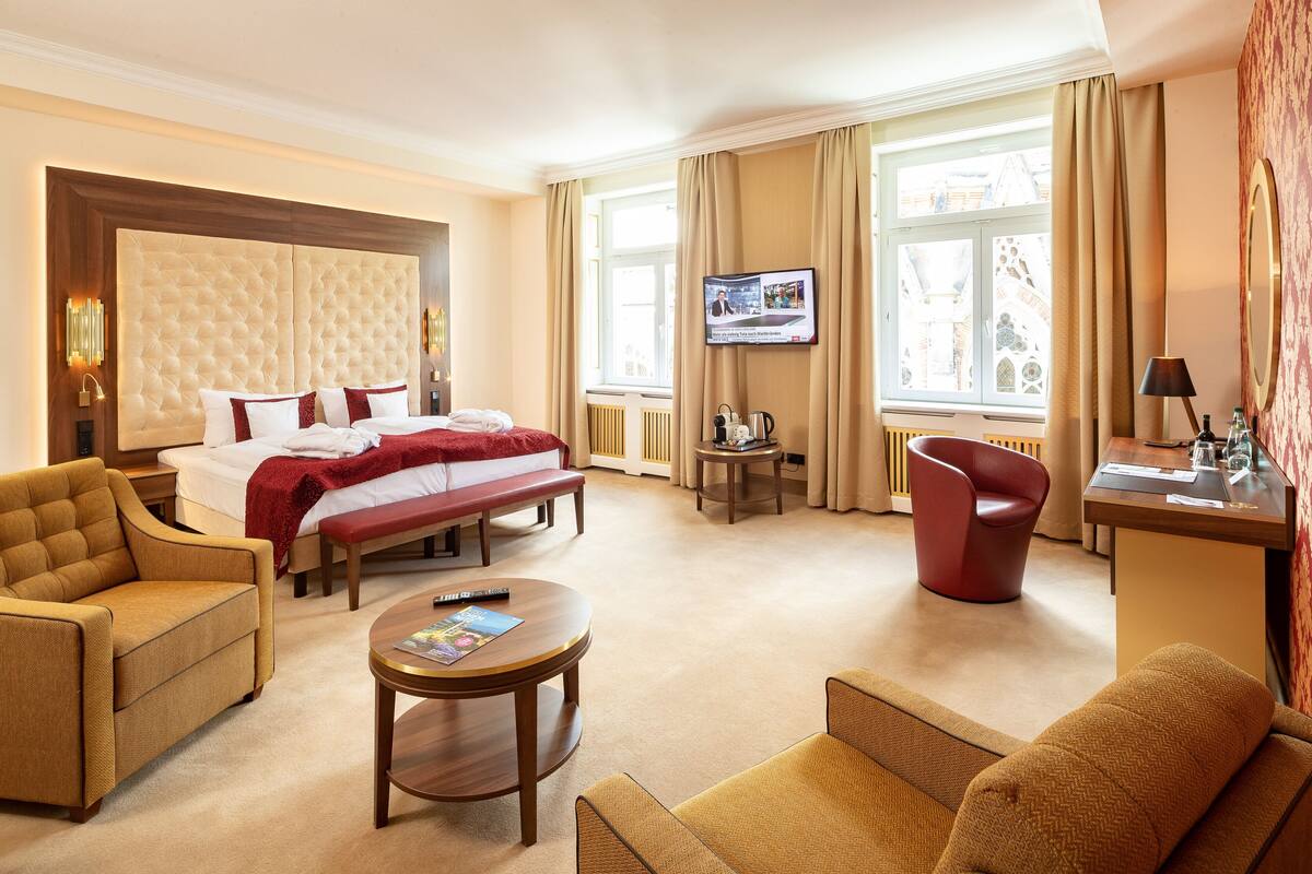 A hotel room with a large bed, a TV, a desk, and a sofa.