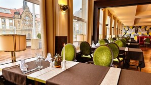 A restaurant with tables set for dining, large windows, and a view of a historic building. - Hotel Chemnitzer Hof (Chemnitz)