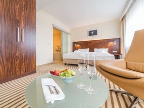 A hotel room with a bed, a sitting area with a glass table, and a wooden wardrobe.