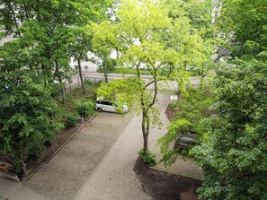A parking area with a white car, surrounded by trees and a paved walkway.