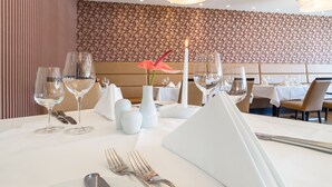 A restaurant setting with a table set for dining, including wine glasses, cutlery, and a vase with a flower.