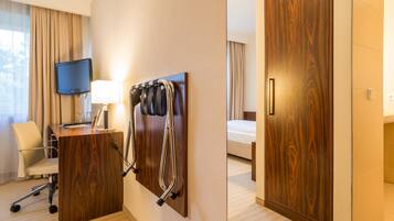 Ein Hotelzimmer mit Holztisch, Fernseher, Schreibtischlampe, Stuhl, Bett und Kleiderschrank.