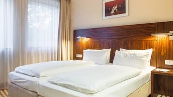 Ein Hotelzimmer mit zwei Betten, einem Holzkopfteil, einem gerahmten Bild an der Wand und einem Fenster mit durchsichtigen Vorhängen.