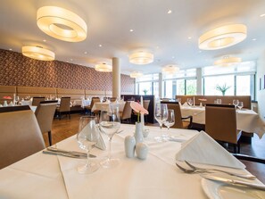 A restaurant with round ceiling lights, white tablecloths, and floral centerpieces.