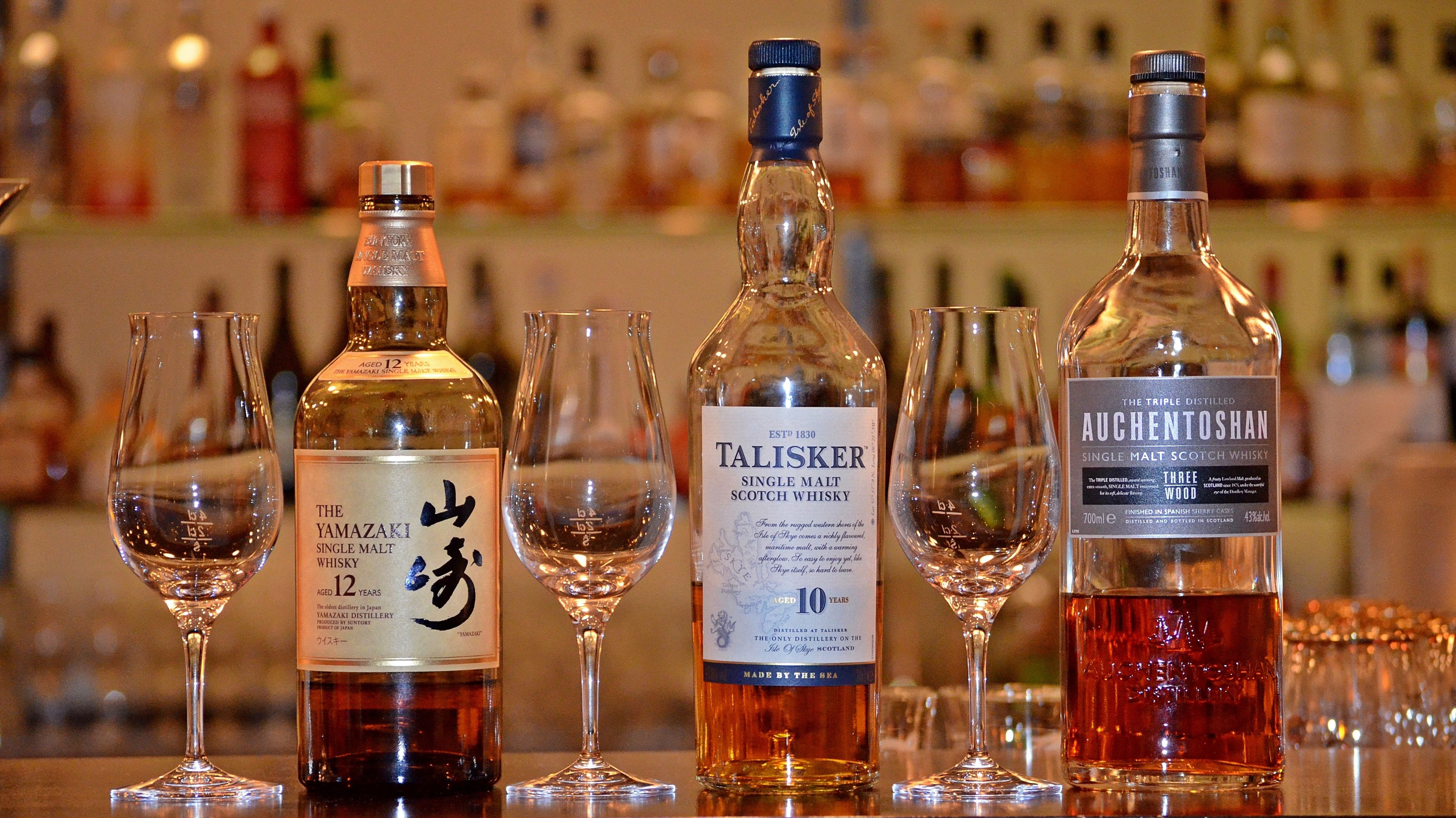 A selection of whisky bottles and glasses on a bar counter.
