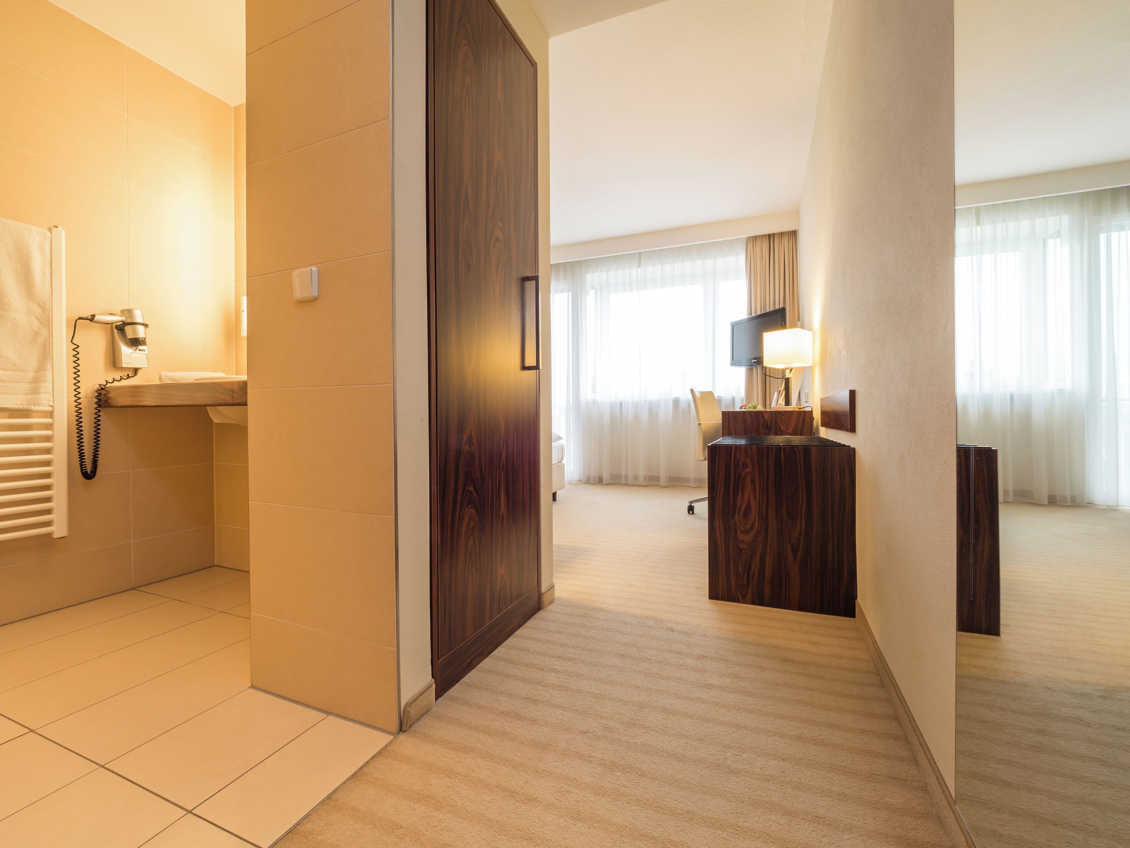 Ein Hotelzimmer mit Bad, Schreibtisch, Stuhl, Fernseher und einem großen Fenster mit Vorhängen.