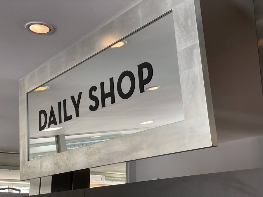 Ein Schild mit dem Text "DAILY SHOP" vor einem modernen Gebäude im Industriedesign.