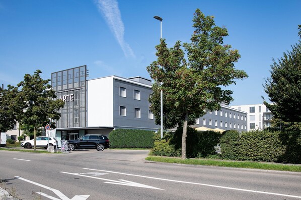 A modern building with a large glass facade, a parking area, and a clear sky.