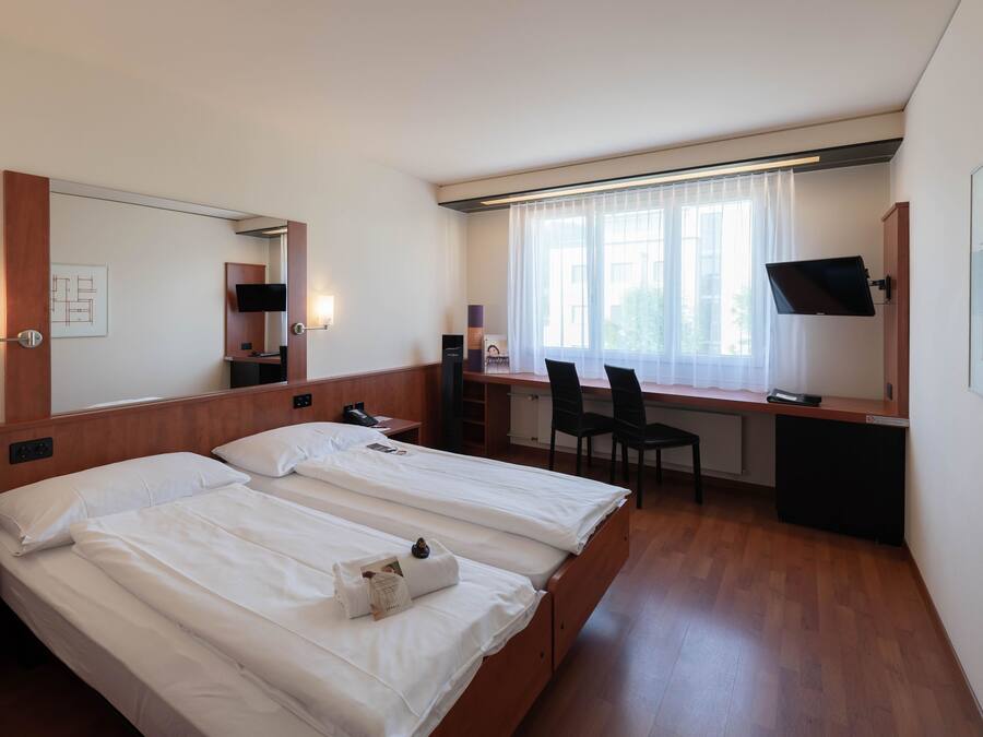 Hotelkamer met twee bedden, een bureau, een stoel, een televisie en een raam met gordijnen.