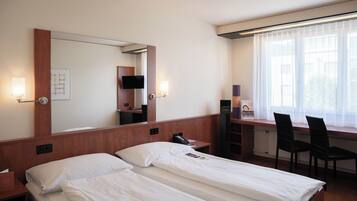 A hotel room with two beds, a desk, a chair, a mirror, and a window with curtains.