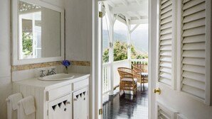 Un baño con lavamanos, espejo y toallero blancos. Se ve un balcón con sillas de mimbre y una mesa.