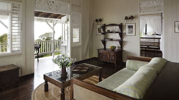 A cozy living room with a sofa, a coffee table with a vase, a wooden cabinet, and a bookshelf. There is a balcony with a railing and a bench.