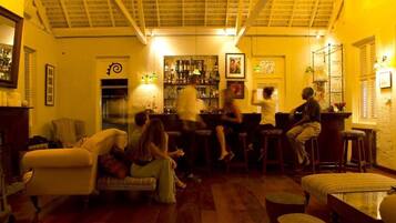 A cozy bar area with wooden floors, a bar counter, and stools. There are chairs and a sofa in the seating area.