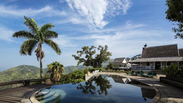 Un resort con piscina cristalina, palmeras y vistas a las montañas.