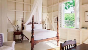 Un dormitorio con cama con dosel, una mesita de noche, una silla, un ventanal con persianas y vistas al exterior.