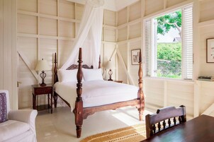 Un dormitorio con cama con dosel, una mesita de noche, una silla, un ventanal con persianas y vistas al exterior.