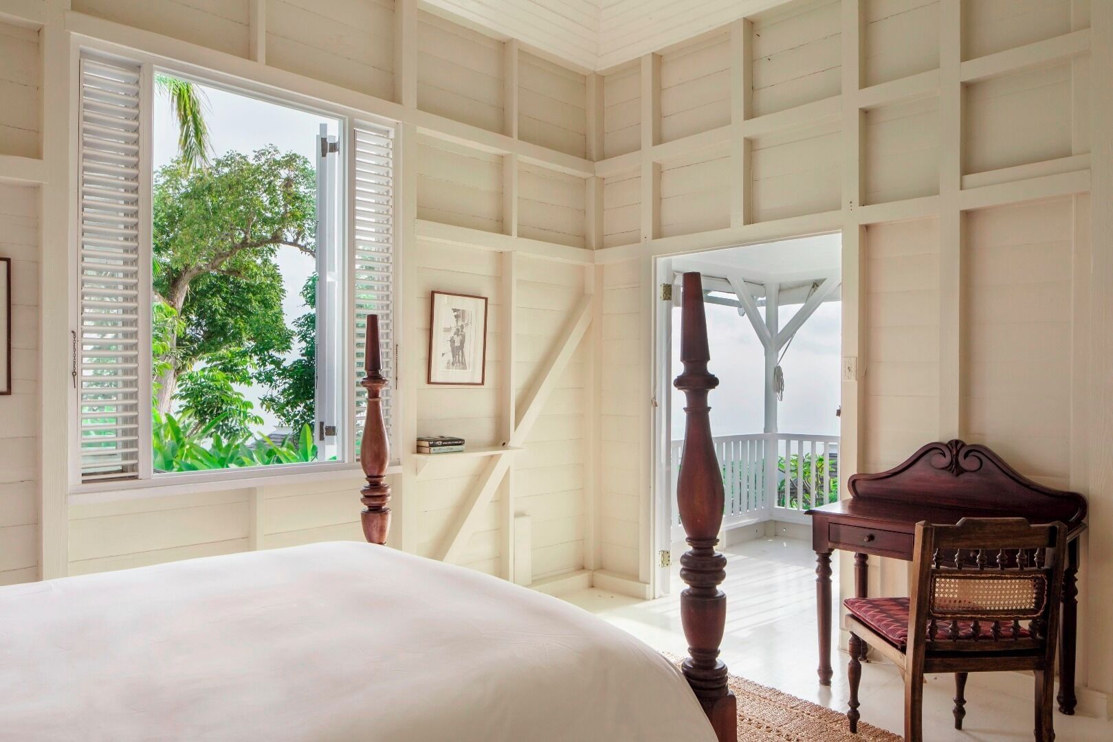 Quarto com uma cama grande, uma cadeira de madeira e vista para o verde lá fora.