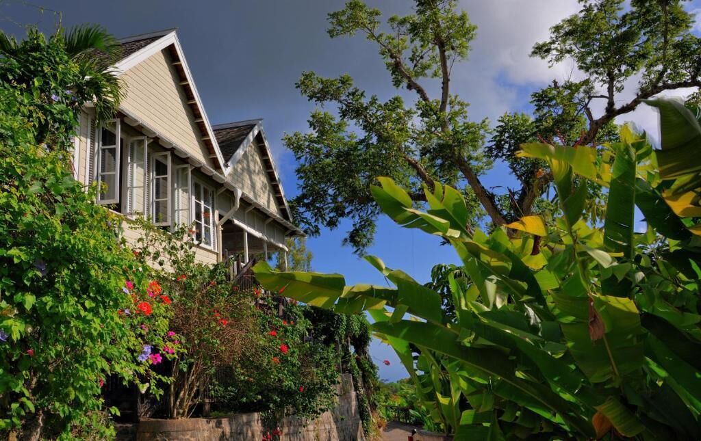 Une maison traditionnelle avec un toit en pente, entourée d’une végétation luxuriante et de plantes en fleurs.