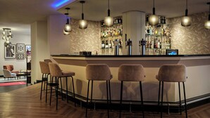 Zona de bar con mostrador, taburetes, lámparas colgantes y una pared llena de botellas de licores.