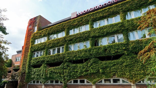 Un edificio con fachada cubierta de hiedra verde y un cartel de hotel visible.