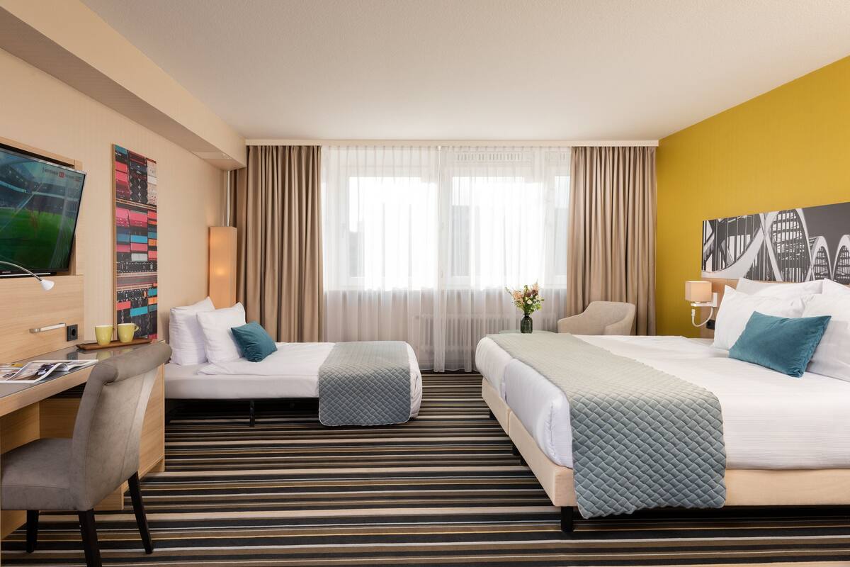 Une chambre d’hôtel avec deux lits, un bureau, une chaise, une télévision et une fenêtre avec des rideaux.