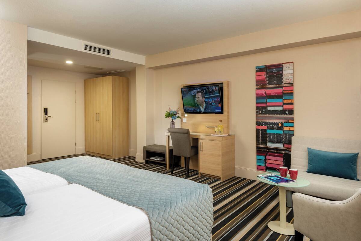 Ein Hotelzimmer mit zwei Betten, einem Schreibtisch, einem Fernseher und einem farbenfrohen Wandbild.