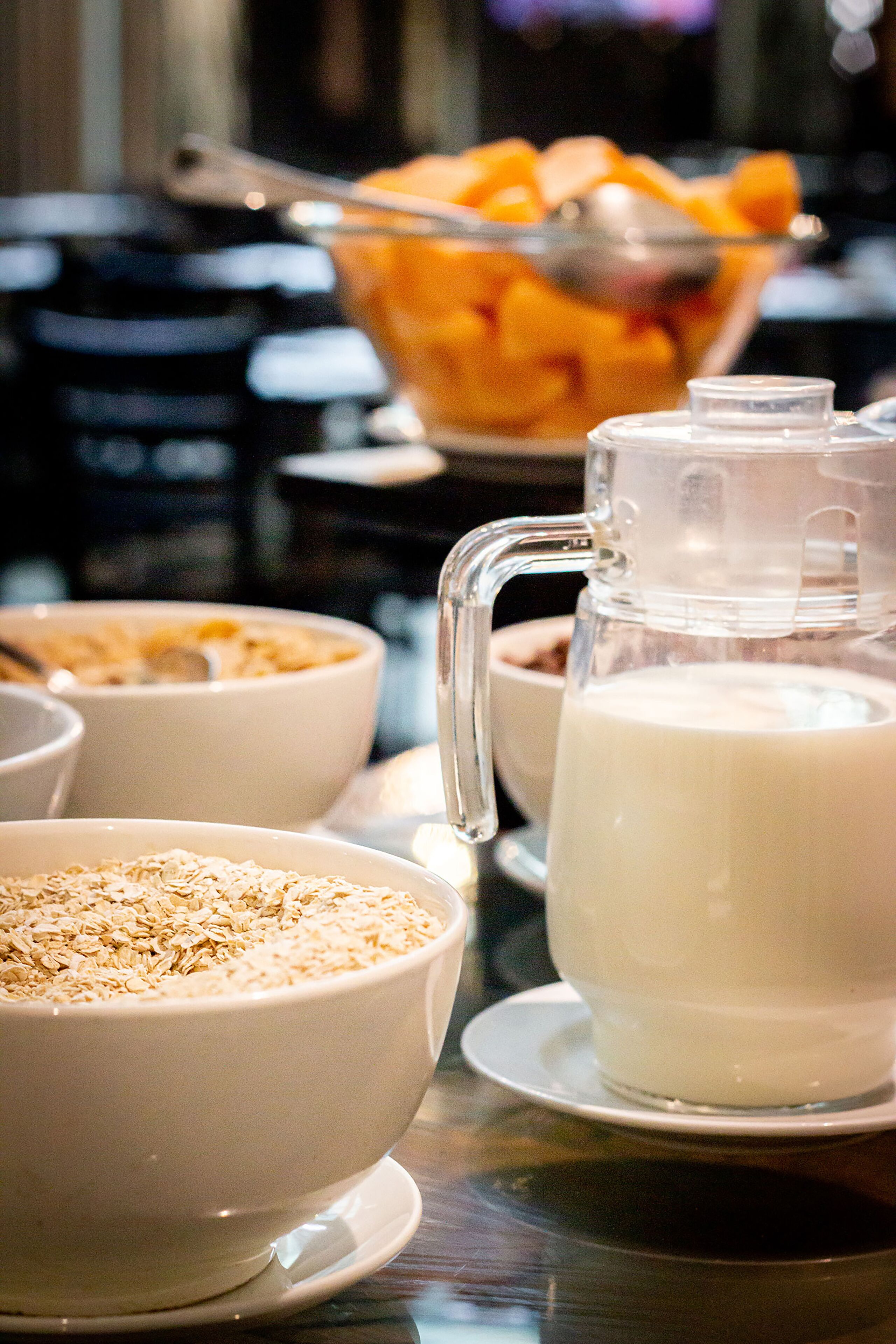 Desayuno con tazones de cereal y leche, una jarrilla y un bol de fruta.