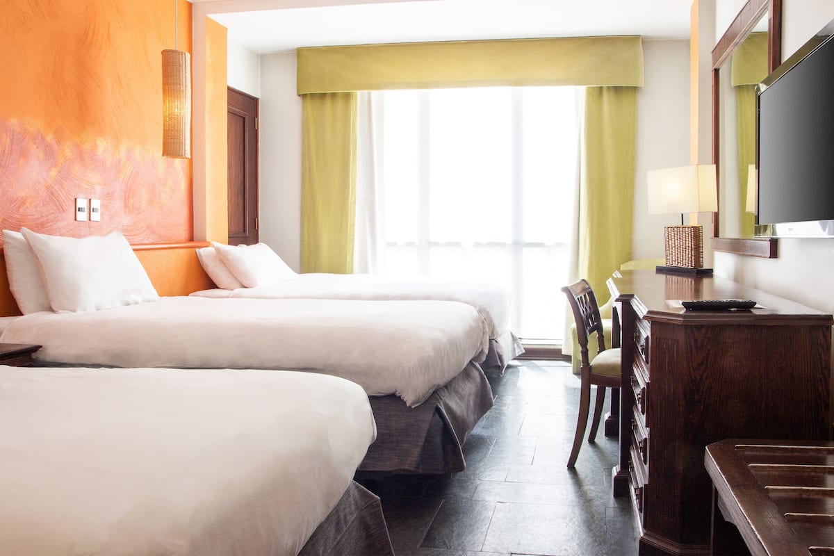 A hotel room with two beds, a desk, a chair, and a TV.