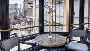 A balcony with two chairs and a small table, a vase with flowers, and a view of the cityscape. - Hotel Fundador (Santiago)