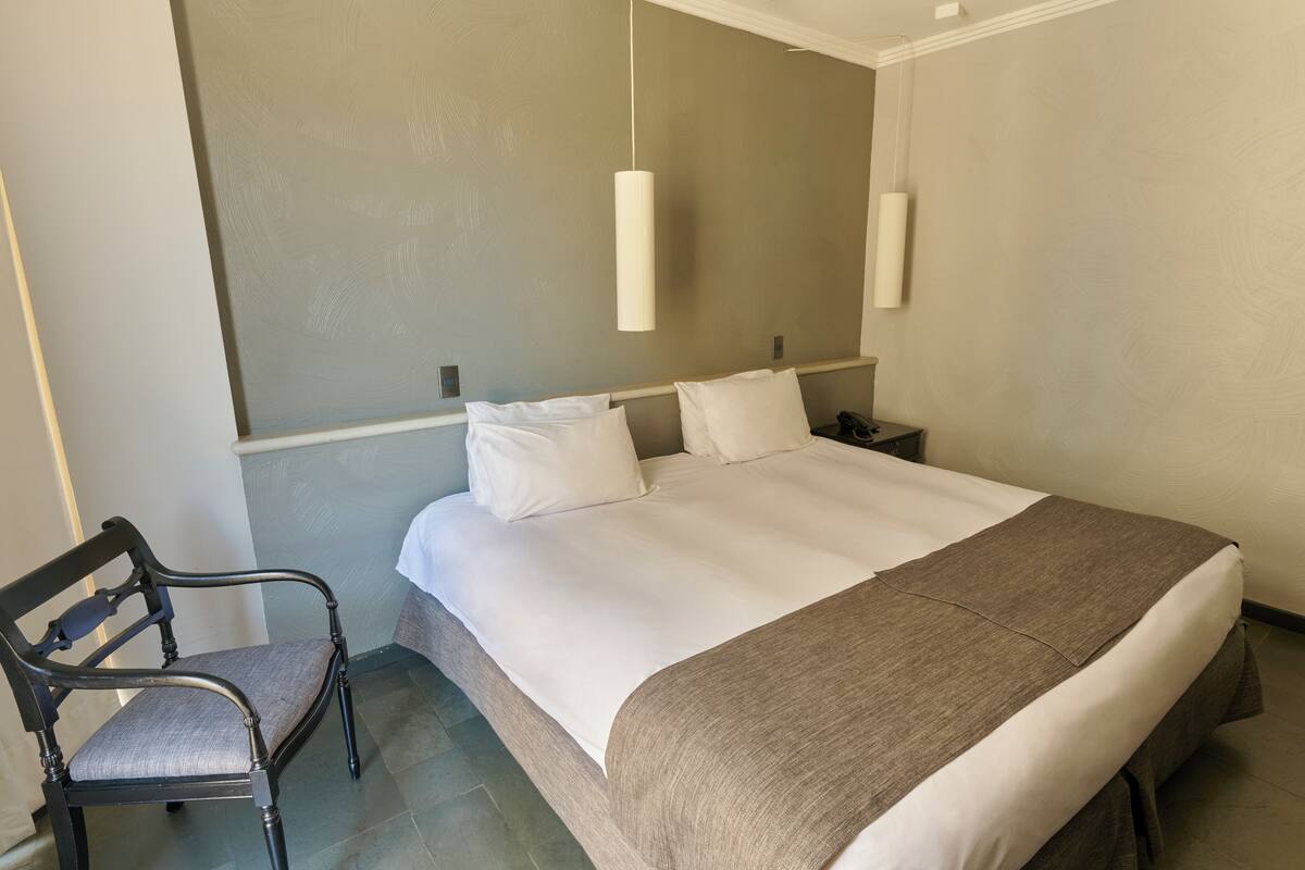 A hotel room with a large bed, a chair, a nightstand, and a hanging light fixture.