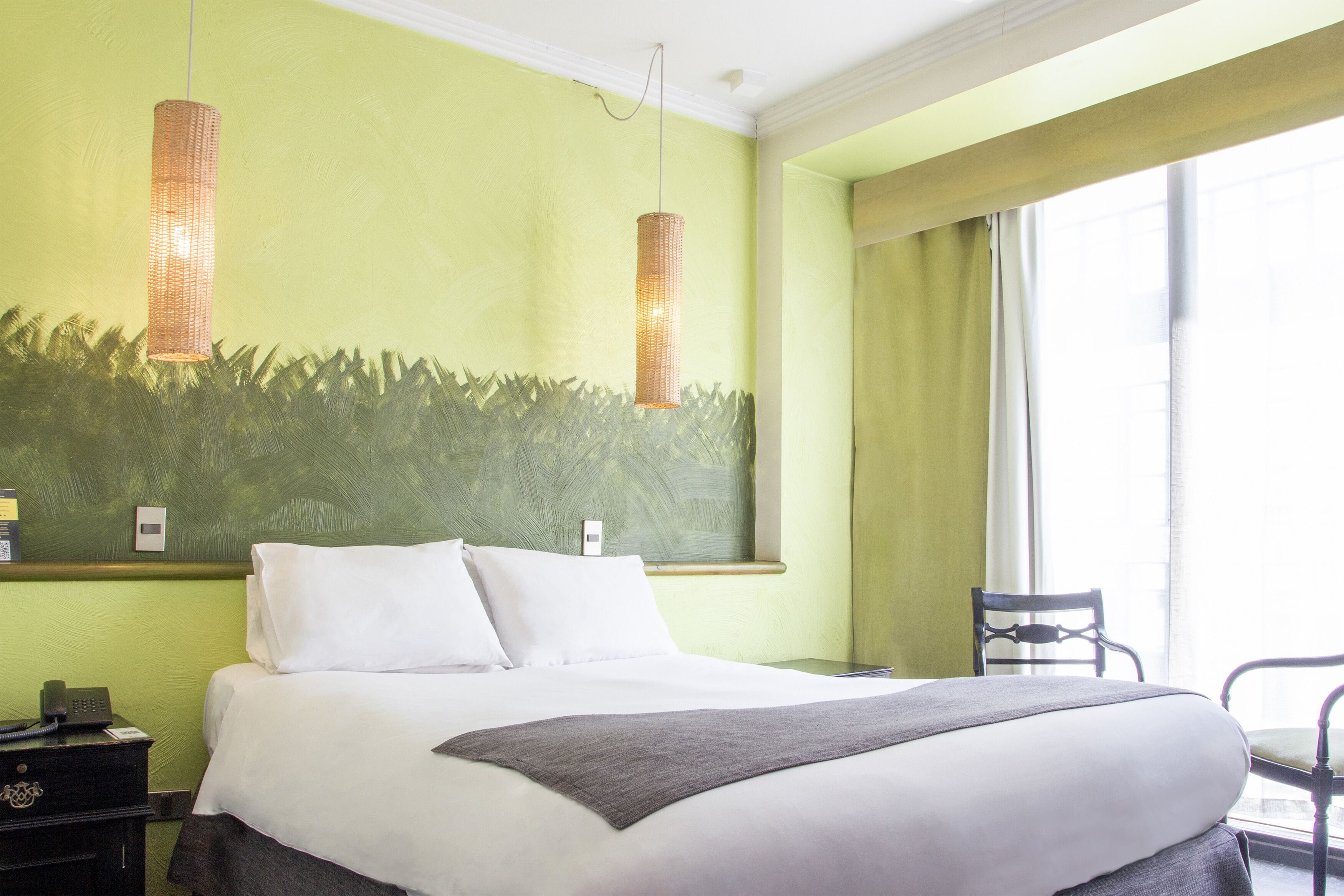 Habitación de hotel con una cama grande, una mesita de noche, una silla y una ventana con cortinas.