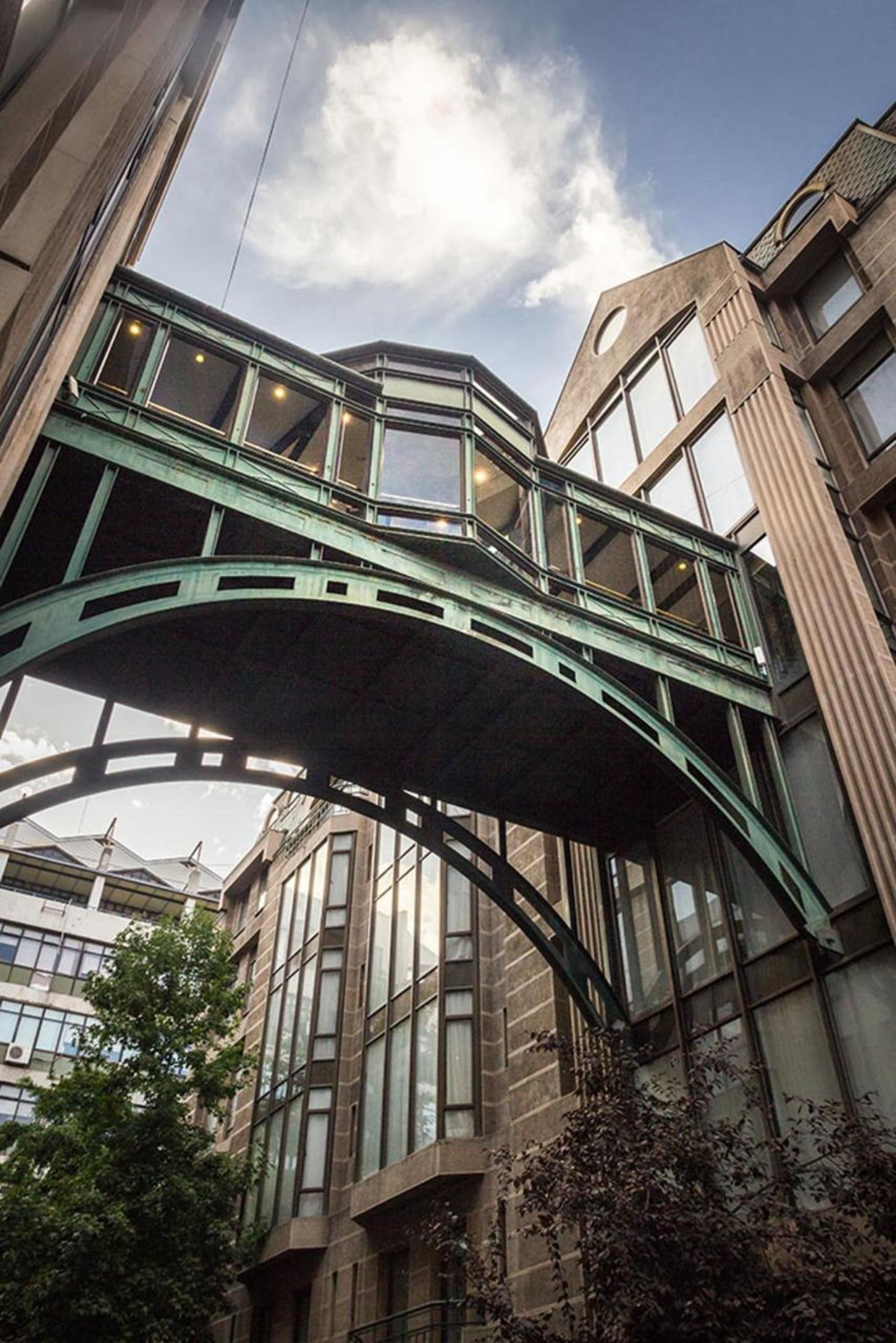 Un edificio de varios pisos con un puente peatonal verde que conecta las plantas.
