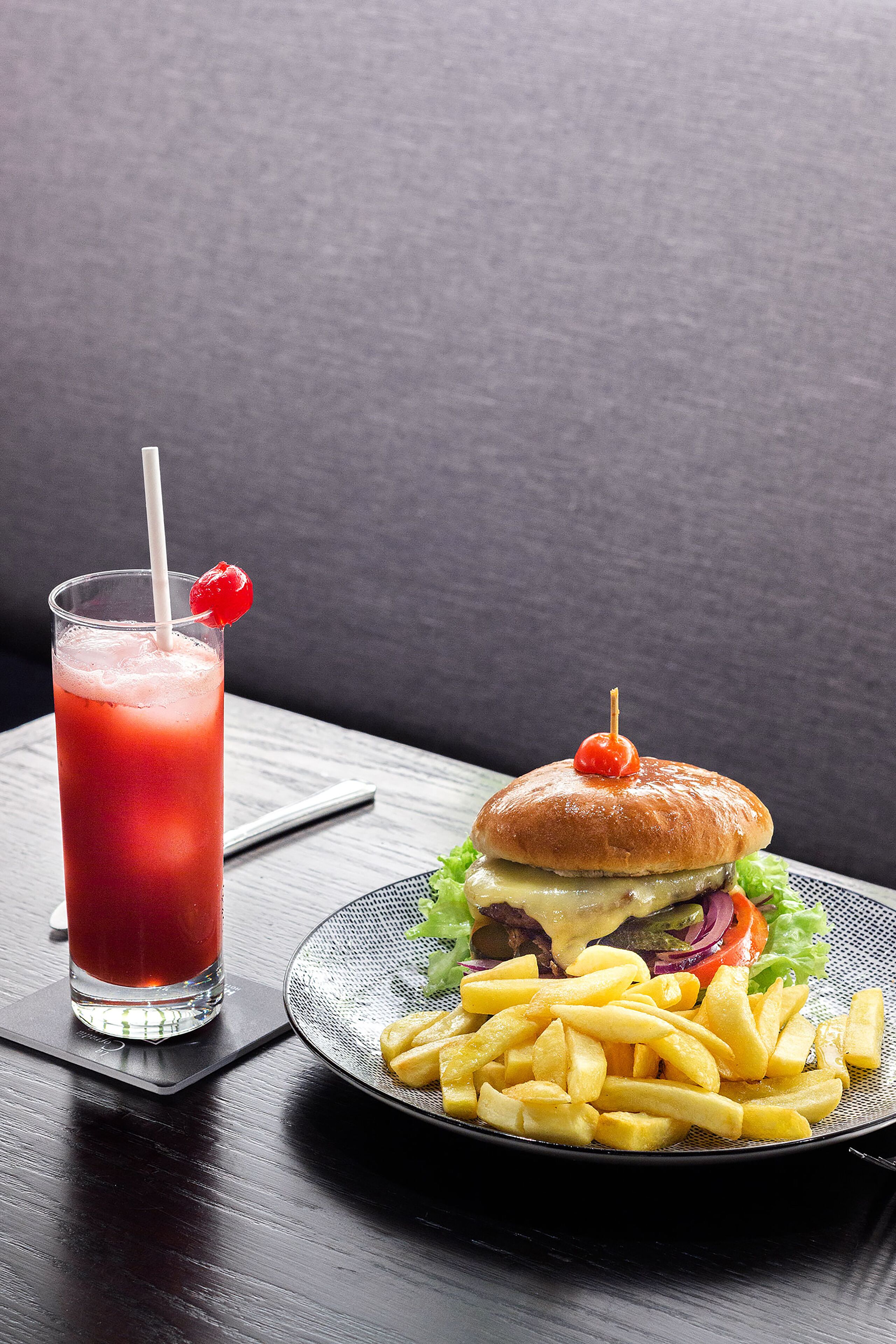 A meal consisting of a burger, fries, and a glass of red drink with a straw and cherry on the side.