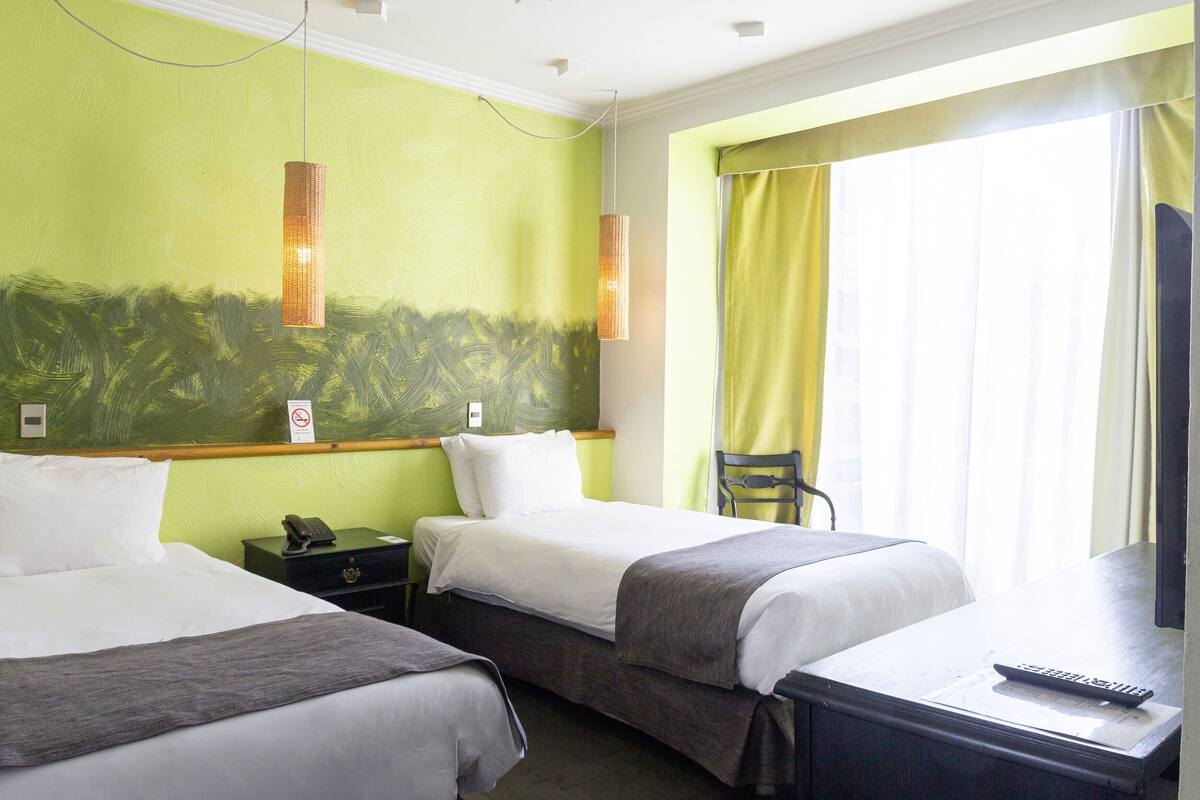 A hotel room with two beds, a desk, a chair, a TV, and a window with curtains.