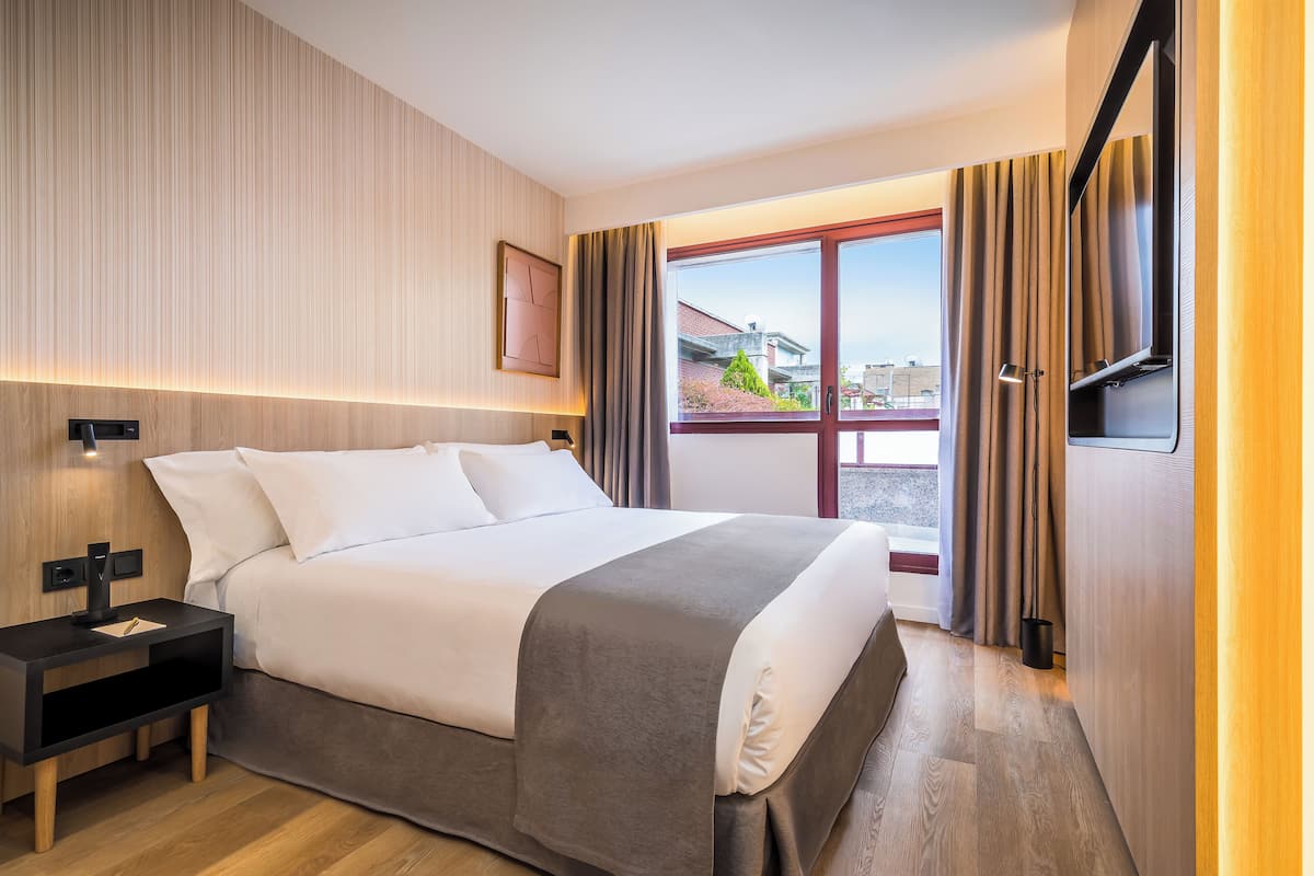 Una habitación de hotel moderna con una cama grande, mesitas de noche, un televisor y una ventana con cortinas.