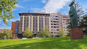 A multi-story building with a modern architectural design, featuring a mix of rectangular and curved windows, and a prominent sculpture in the foreground.