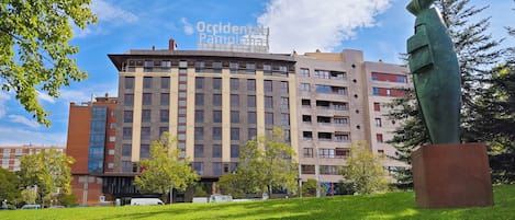 A multi-story building with a modern architectural design, featuring a mix of rectangular and curved windows, and a prominent sculpture in the foreground.