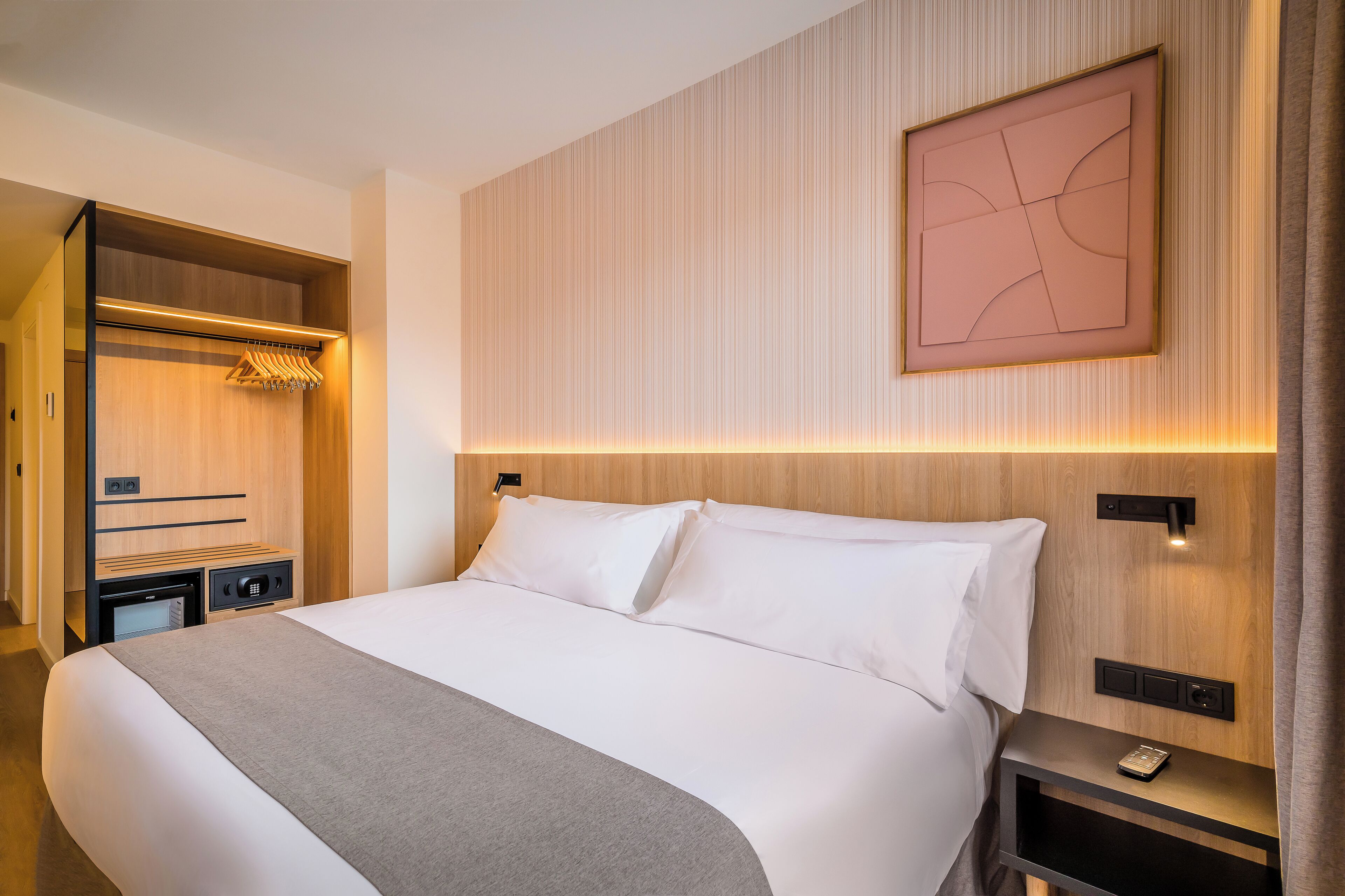 Habitación de hotel con una cama grande, un armario de madera, una mesita de noche con teléfono y una obra de arte colgada en la pared.