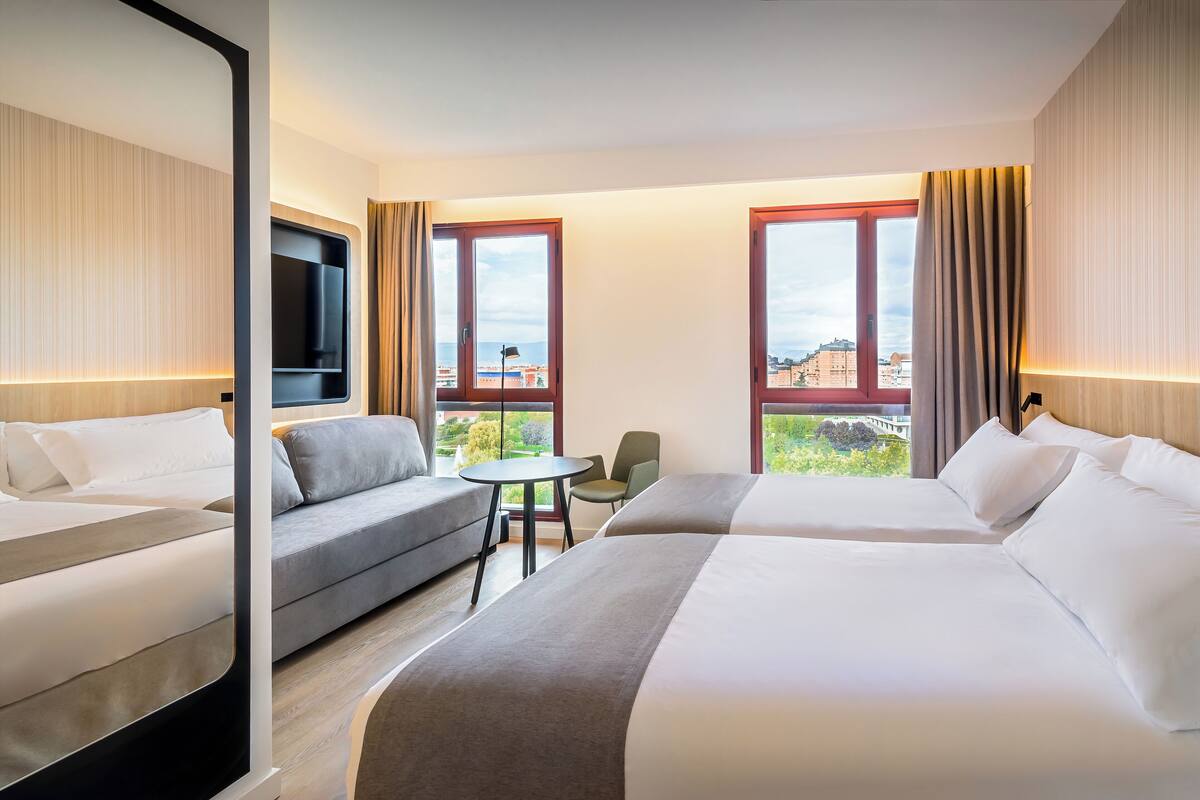 Habitación de hotel con dos camas, un sofá, una mesita y un televisor.