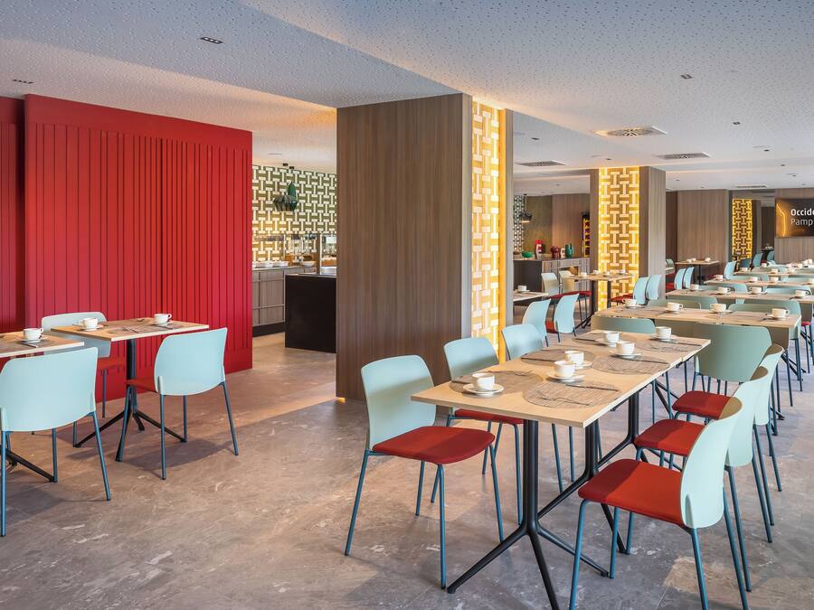 A modern restaurant with long communal tables and individual chairs, featuring a mix of red and light blue colors.