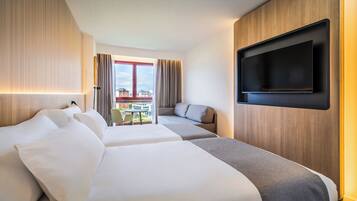 Habitación de hotel con dos camas, un televisor montado en la pared y un balcón con vistas a la ciudad.