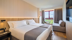 A hotel room with two beds, a sofa, a small table, and a window with a view.