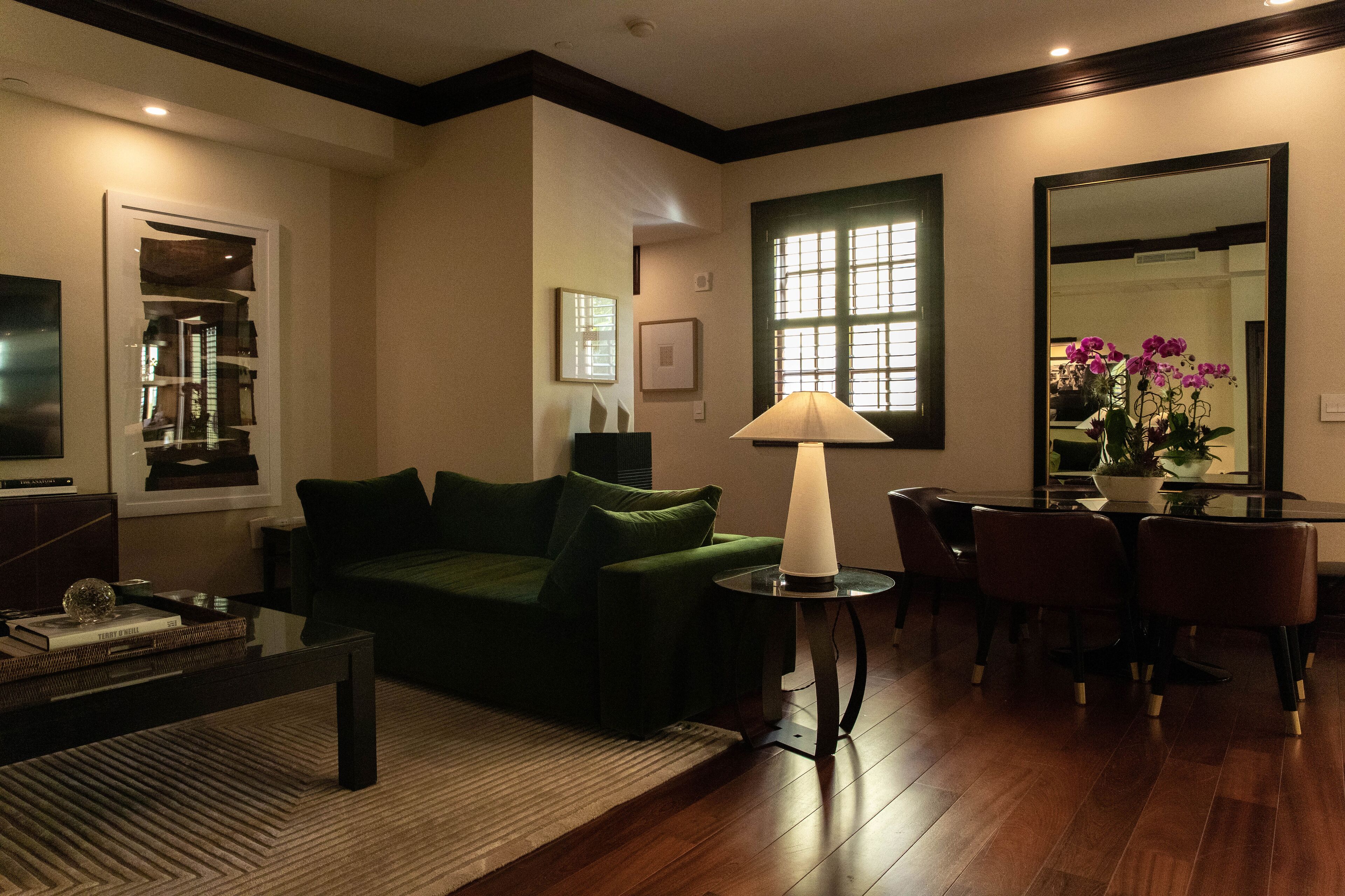 Uma sala de estar com um sofá verde, uma mesa de centro, uma luminária e uma área de jantar com cadeiras e uma mesa.