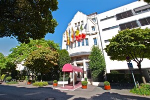 A hotel entrance with a red canopy, potted plants, and flags.
